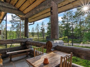 A rustic wooden cabin with a large log table and benches, surrounded by a forest.