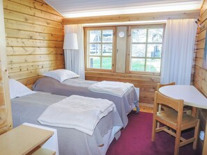 A wooden cabin room with two beds, a table, and a window with curtains.