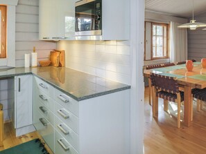 A kitchen with a built-in microwave, a wooden dining table with chairs, and a view of the outdoors through a window.