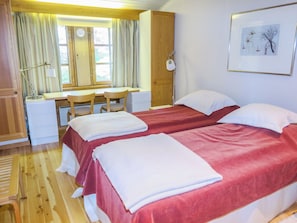 Et hotelværelse med to senge, et skrivebord, stole og et vindue med gardiner.