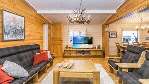 Un intérieur de chalet chaleureux, avec un revêtement mural en bois, un ensemble de canapés, un coin repas et un téléviseur.