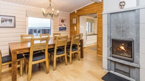 Un coin repas avec des chaises et une table en bois, une cheminée et une vue sur l’extérieur.