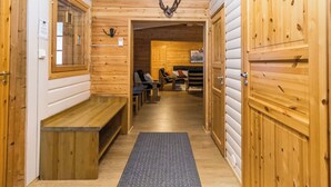Un intérieur en bois avec un banc, une porte ornée de bois de cerf, et une vue sur une pièce comprenant un lit et une cheminée.