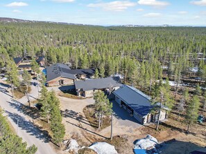 Un quartier résidentiel composé de plusieurs chalets, entouré d’une forêt dense, sous un ciel dégagé, et offrant une vue lointaine sur des collines.
