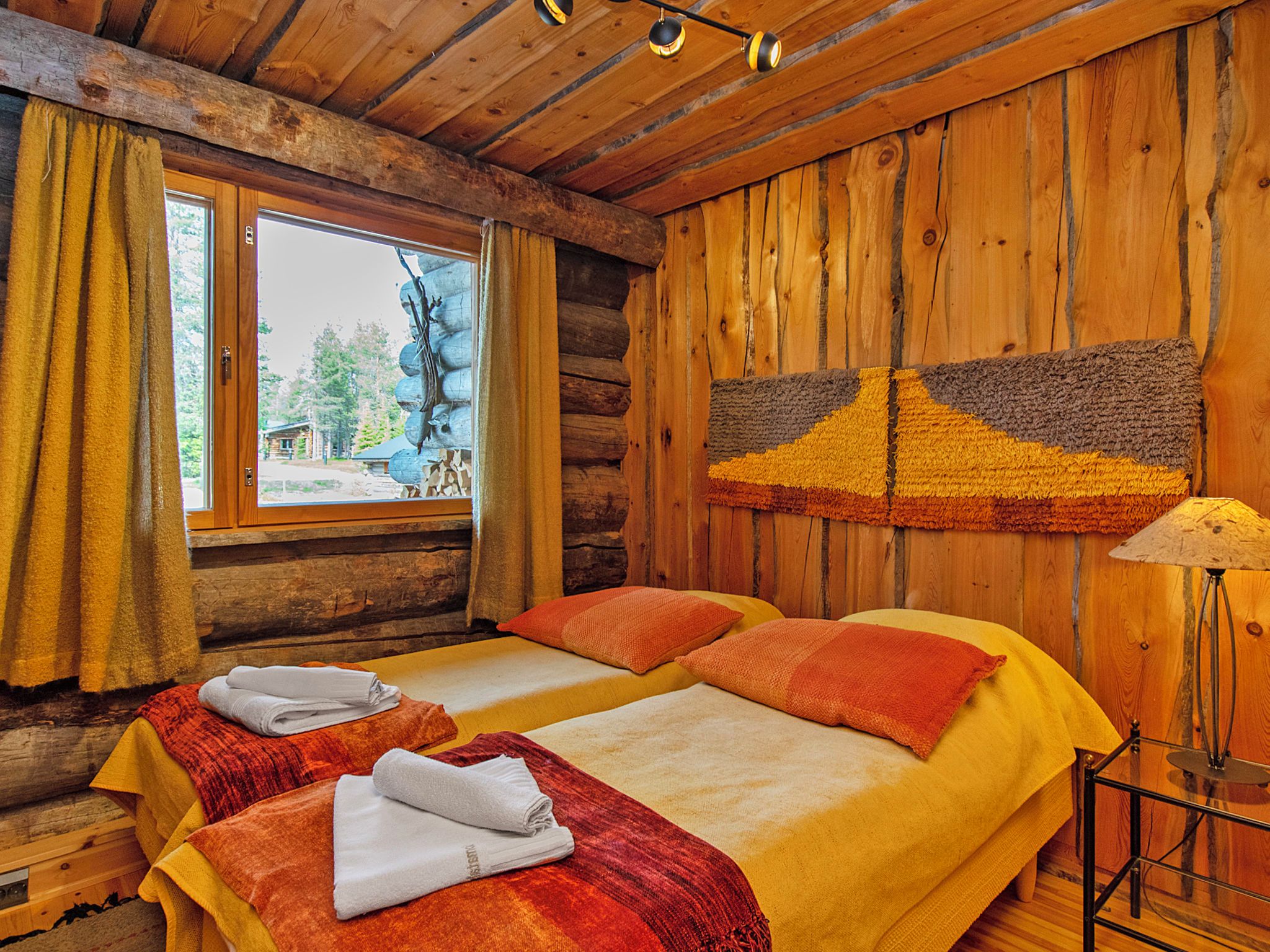 Une chambre de style rustique avec deux lits, une fenêtre avec des rideaux, une lampe et une vue sur un chalet situé à l’extérieur.