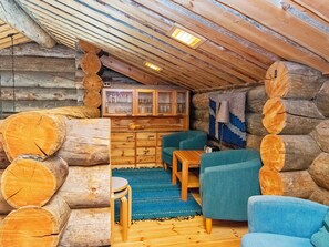 A log cabin interior with a loft area, wooden furniture, and a blue rug.