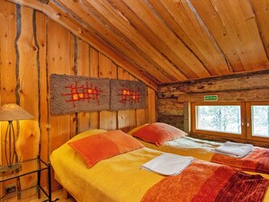 A cabin with two beds, a wooden ceiling, and a window with a view of trees.