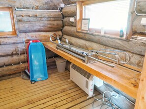 A log cabin interior with a wooden bench, a blue heater, and a window with a view.