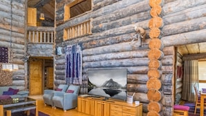 L'intérieur d'une cabane en rondins, avec un téléviseur, des sièges et une cheminée.