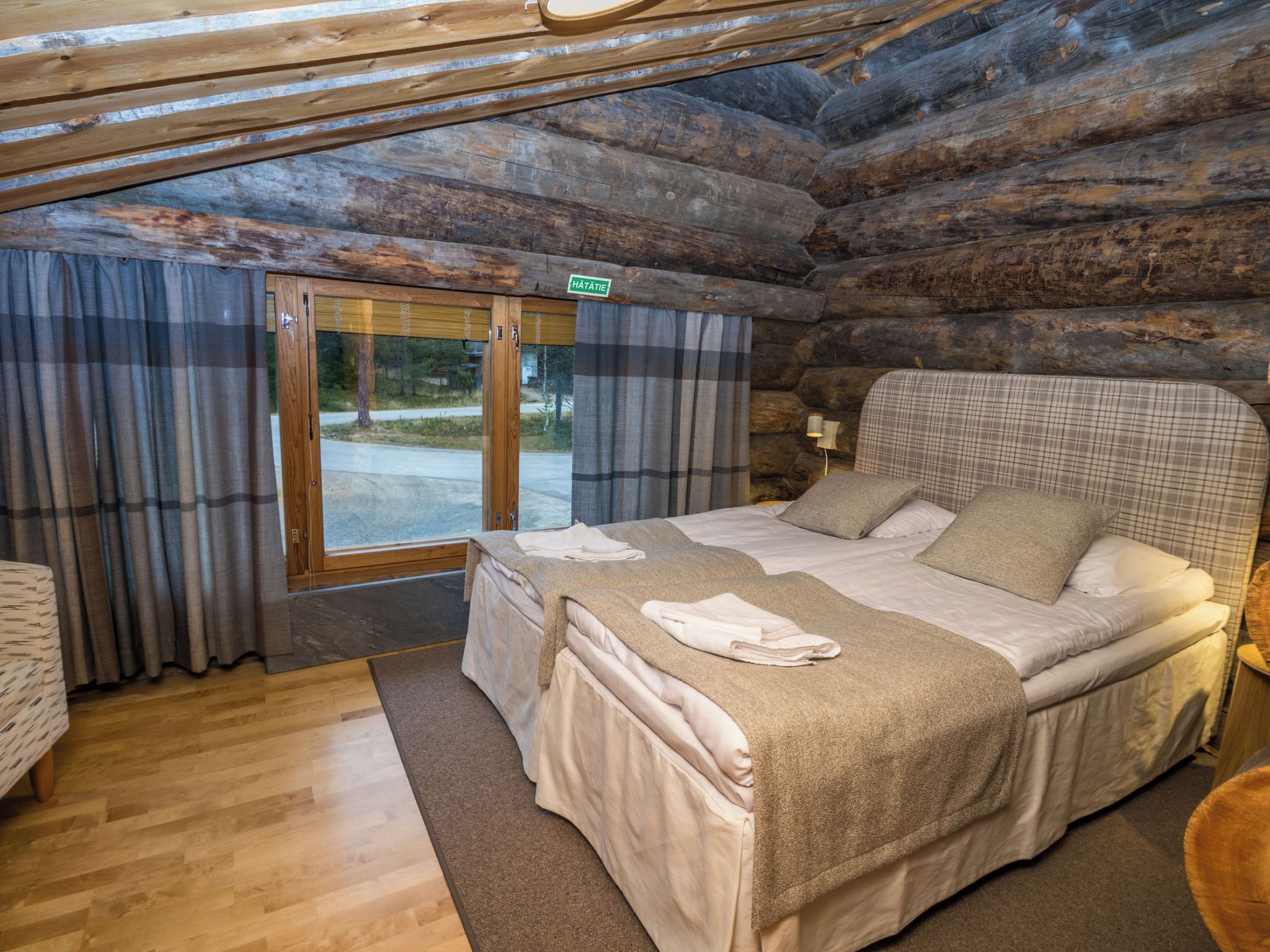 A log cabin bedroom with a bed, curtains, a bench, and a view through a door.
