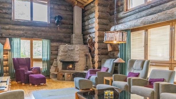 L’intérieur d’une cabane en rondins, avec une cheminée en pierre, plusieurs coins salon et de grandes fenêtres.
