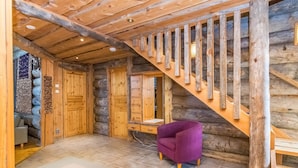 L’intérieur d’une cabane en rondins, avec un escalier en bois, un fauteuil violet et un sol carrelé.