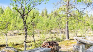 A rustic outdoor setting with a stack of firewood and logs, surrounded by trees and a clear sky. - Oton kämppä by Interhome (Inari)