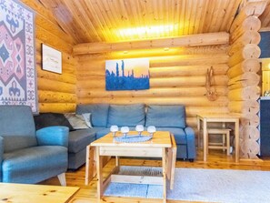 Interior de una cabaña de madera con un sofá, una mesa de centro con vasos y un cuadro en la pared.