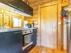 Eine kleine Küche mit Holzausstattung, integriertem Backofen, Kaffeemaschine und Kühlschrank.