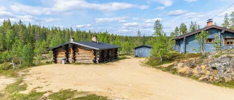 A log cabin with a dirt driveway leading to a wooden structure.