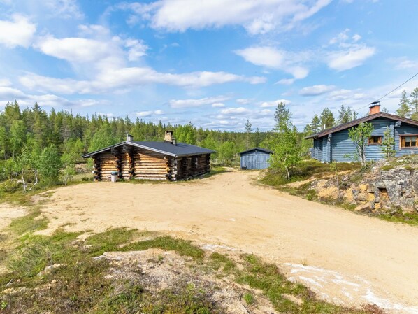 A log cabin with a dirt driveway leading to a wooden structure.
