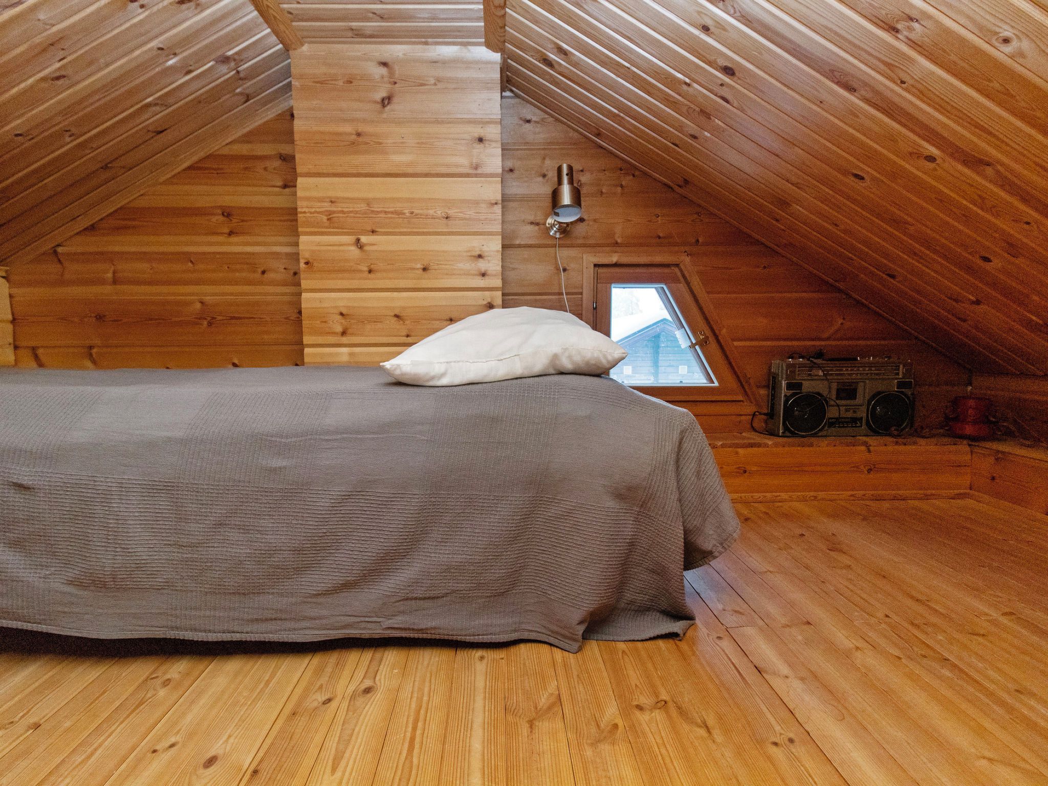 A cozy attic bedroom with a wooden floor, a bed with a pillow, a window, and a vintage radio.