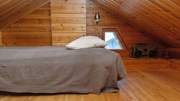 A cozy attic bedroom with a wooden floor, a bed with a pillow, a window, and a vintage radio.