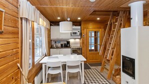 A compact kitchen with white cabinets, a dining table with chairs, a built-in microwave, and a stove. - Ressipysäkki 1 by Interhome (Inari)