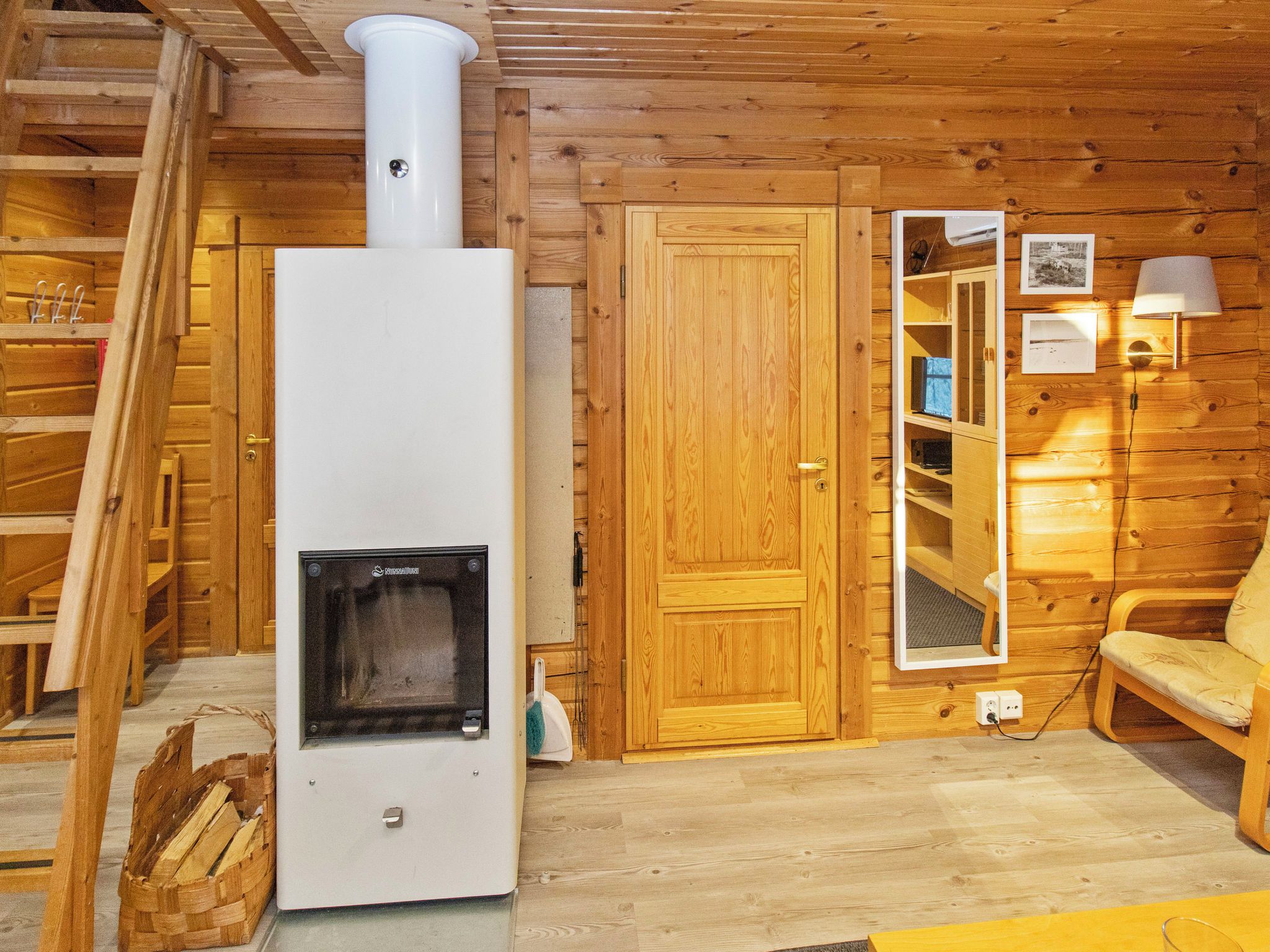 A wooden cabin interior with a wood stove, a door, a mirror, and a chair.