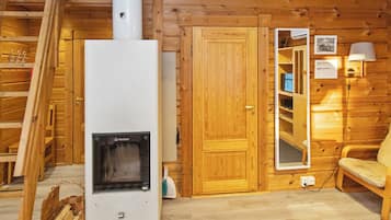 A wooden cabin interior with a wood stove, a door, a mirror, and a chair.