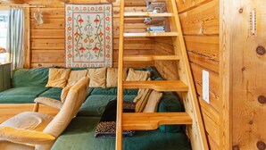 Interior acolhedor de uma cabana com um sofá verde, prateleiras de madeira e um tapete decorativo.