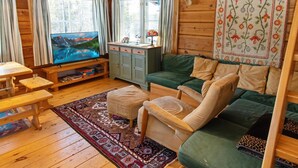 Interior acolhedor de uma cabana com decoração em madeira, um sofá verde, uma televisão e uma mesa pequena.