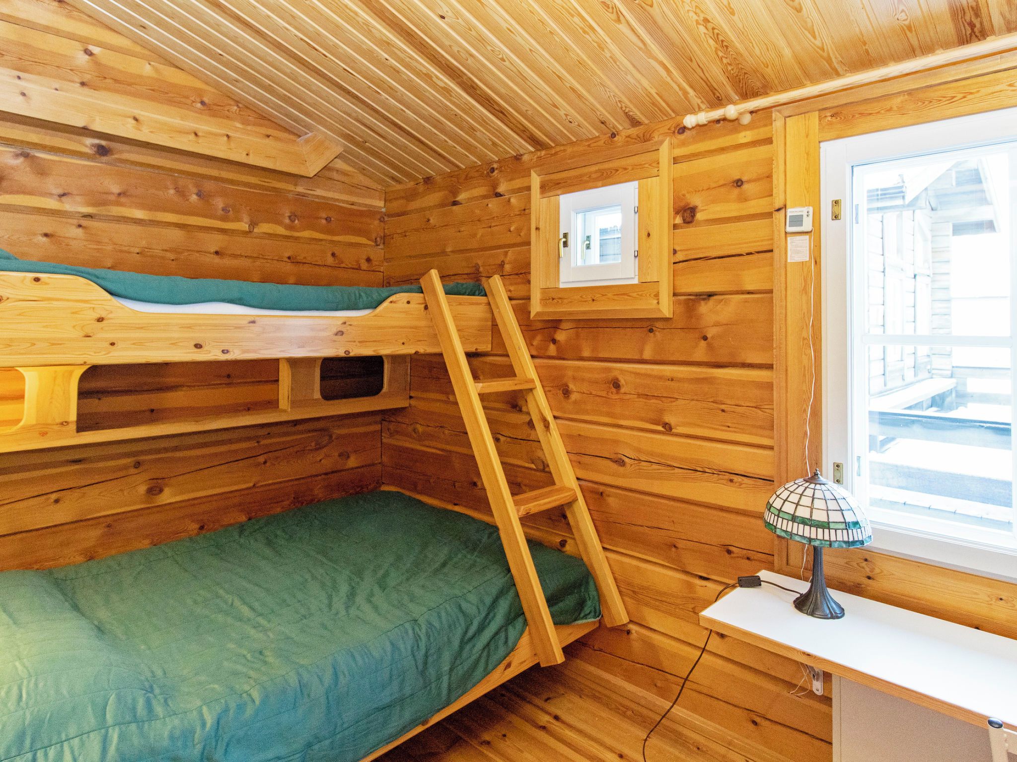 Une pièce en bois aménagée comme une cabine, avec des lits superposés, une échelle, une fenêtre et un bureau avec une lampe.