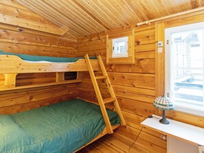 Ein Zimmer in einer Holzhütte mit Etagenbetten, einer Leiter, einem Fenster und einem Schreibtisch mit Lampe.