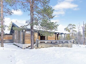 A wooden cabin with a sloped roof, surrounded by snow-covered ground and trees. - Iso-veke by Interhome (Inari)