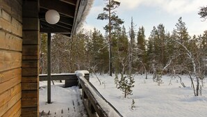 Uma cabana de madeira com um deck coberto de neve e vista para uma floresta.