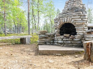 A stone-built outdoor oven in a forested area with a bench nearby.
