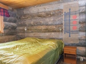 A log cabin room with a bed, a hanging tapestry, and a small wooden nightstand.