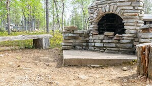 A stone-built outdoor fireplace with a fire pit, surrounded by a natural forest setting. - Laanikelo by Interhome (Inari)
