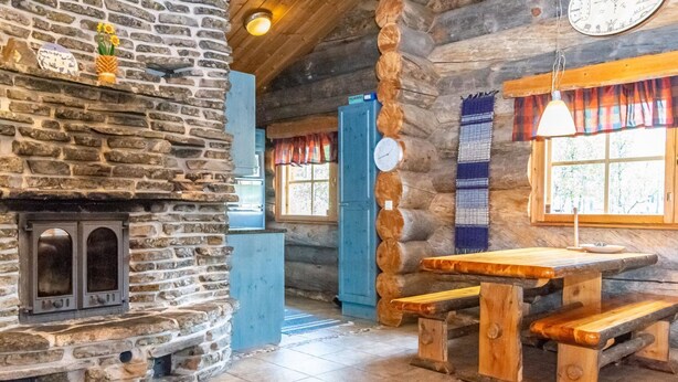 A rustic cabin interior with a stone fireplace, wooden benches, and a clock on the wall. - Laanikelo by Interhome (Inari)