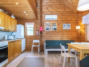 A cozy cabin-style kitchen with wooden walls, a dining area with a table and chairs, and a built-in cabinet with glassware. - Ressipysäkki 2 by Interhome (Inari)