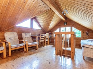 Een knus houten vakantiehuisje met schuine daklijn, ingericht met houten stoelen en een tafel.