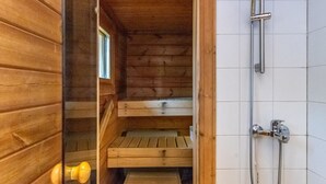 A wooden cabin interior with a shower area, wooden benches, and a window.