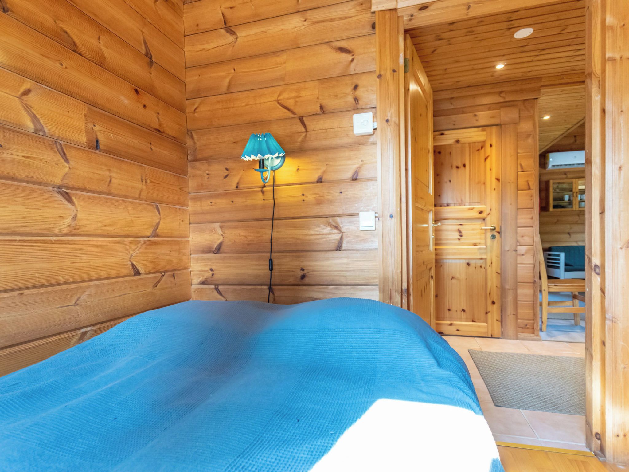 Ein Holzblockhaus im Inneren, mit einem Bett, einer Lampe und einer Tür zu einem Badezimmer.