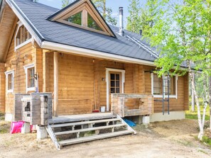 Een houten hut met een puntig dak, een veranda en een schoorsteen.