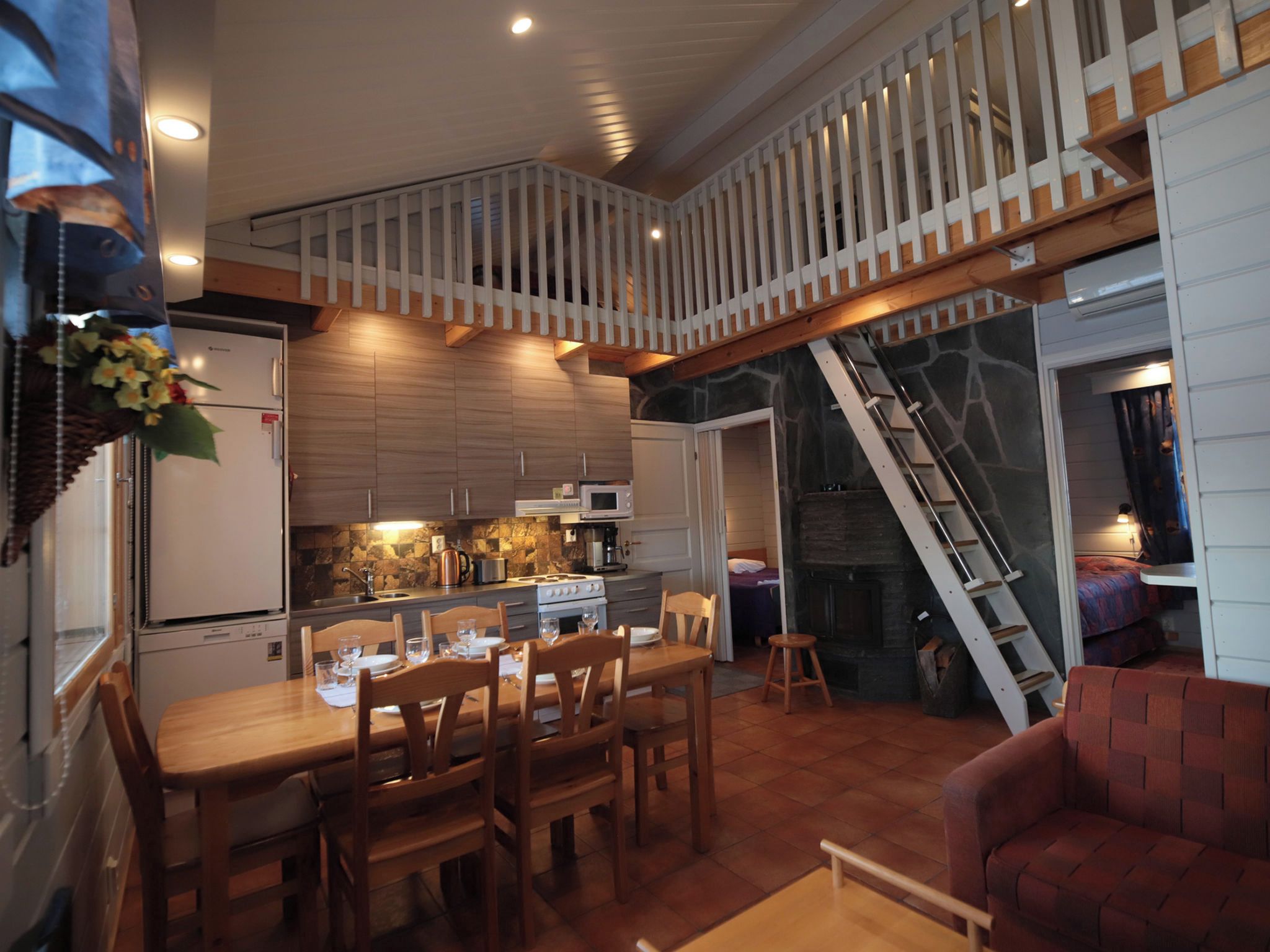 A compact kitchen with modern appliances, a dining area with wooden furniture, and a loft bedroom with a staircase.