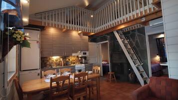 A compact kitchen with modern appliances, a dining area with wooden furniture, and a loft bedroom with a staircase.