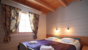 Ein Schlafzimmer mit einem Bett, zwei Nachttischen, einem Fenster mit Vorhängen und Holzbalken an der Decke.