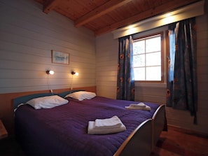 Ein Zimmer mit einem Bett, zwei Wandleuchten, einem Vorhangfenster und einem gerahmten Bild an der Wand.