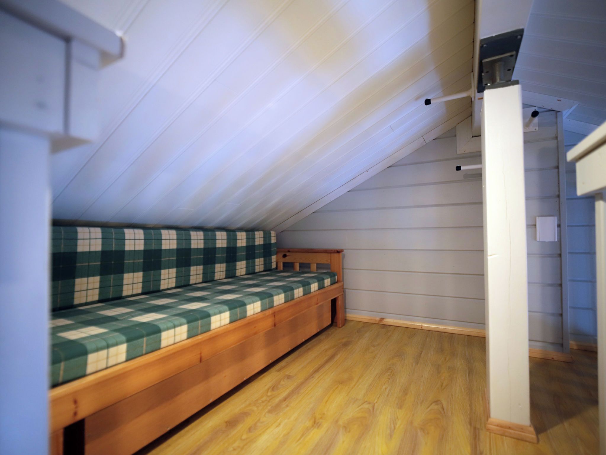 A small, sloped ceiling room with a wooden bench bed and a white wall.