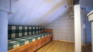 A small, sloped ceiling room with a wooden bench bed and a white wall.