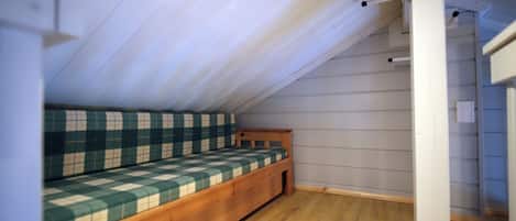 Une petite pièce avec un plafond en pente, un lit en bois et un mur blanc.