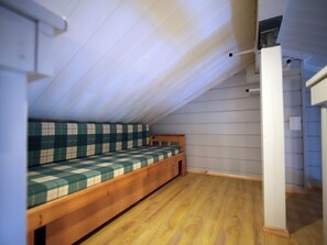 Une petite pièce avec un plafond en pente, un banc-lit en bois et un mur blanc.