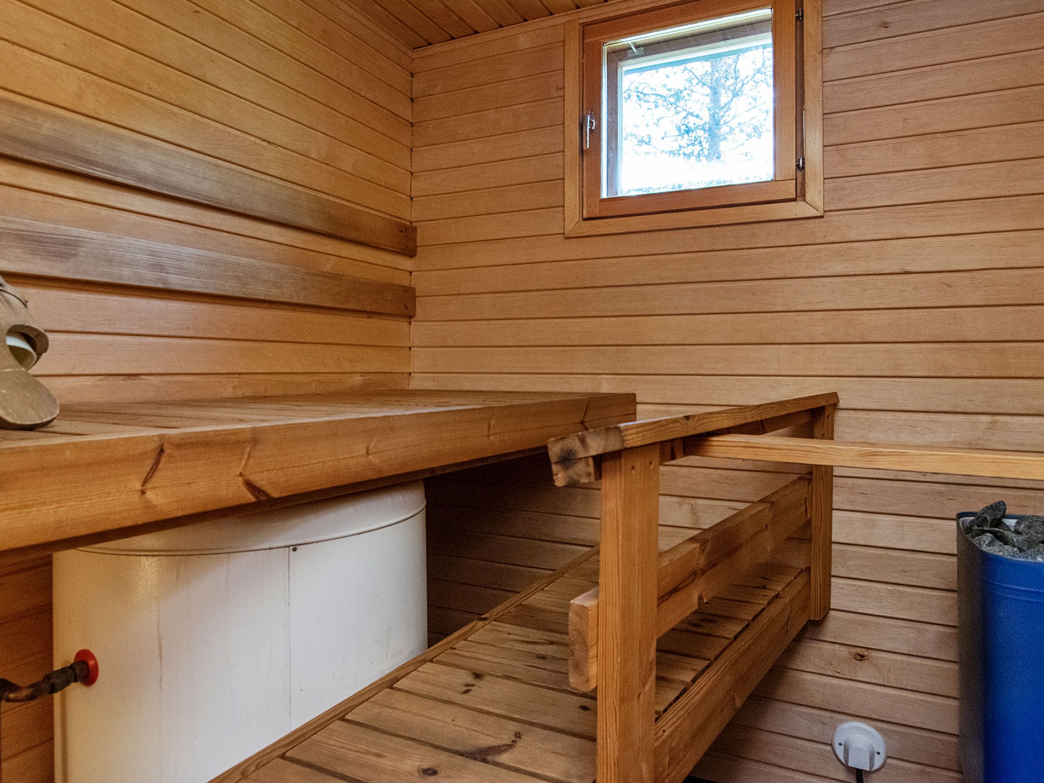 Interior de una cabaña de madera con un banco, una ventana y un cubo de basura.